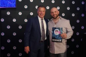 Two men in formal wear pose for a photo at the Long Island Choice Awards; the man on the right holds a WINNER certificate.
