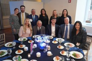 Group of twelve professionally dressed people posing around a round banquet table with plates of salad and bread, a glowing centerpiece that reads 'Top Lawyers of Long Island' in the middle.