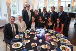 Group of professionally dressed people posing at a round banquet table during a formal event, with a glowing 'Top Lawyers' centerpiece.