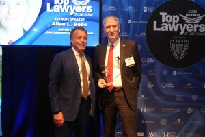 Two men in suits posing on stage at a Top Lawyers of Long Island event; one holds a glass award.