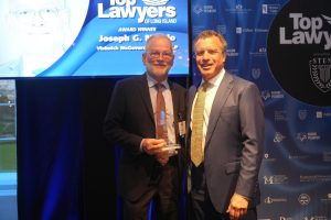 Two men in suits pose on stage at a Top Lawyers awards event; one holds a glass trophy beside the other smiling man.