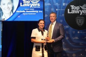 Woman and man on stage holding a glass award at the Top Lawyers of Long Island event with a blue backdrop.