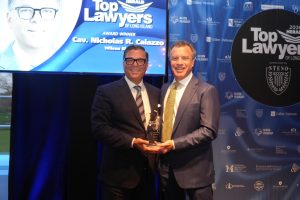 Two men in suits posing with a glass award at a 'Top Lawyers of Long Island' event, blue backdrop with sponsor logos.