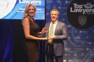 Two professionals on a stage exchange a glass award during a Top Lawyers event on Long Island, with a blue backdrop behind them.