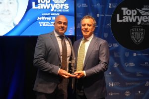 Two men in suits pose on stage with a glass 'Top Lawyers' award against a blue sponsor backdrop.
