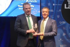 Two men in dark suits pose on stage, holding a glass award at a law awards ceremony.