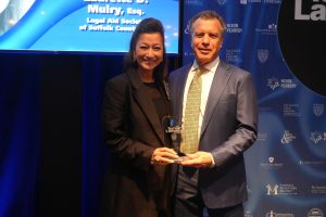 Two professionals in formal attire pose on stage, holding a glass award reading 'Top Lawyers' at a blue-lit awards event.