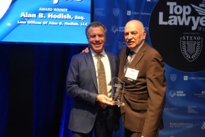 Two men in suits pose on stage at a Top Lawyers awards event; one hands the other a glass trophy as they smile.