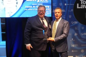 Two suited men at an awards ceremony pose with a glass trophy that reads 'Top Lawyers,' against a blue backdrop filled with sponsor logos.