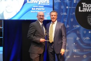 Two men in suits pose on stage at a law awards event, one holding a glass trophy.