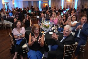 Guests at a banquet clapping around a round table with a floral centerpiece, at a formal event ballroom scene (table 3)