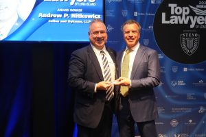 Two men in suits smile as they exchange a glass award onstage at a 'Top Lawyers of Long Island' event.