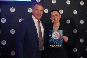 Man in a blue suit and patterned tie stands beside a woman in a black pinstripe suit, holding a 'WINNER' award plaque for the Long Island Choice Awards.