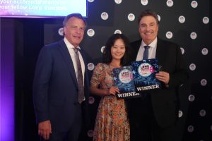 Three winners pose with awards at a Long Island Choice Awards event; woman in a floral dress stands between two men in suits, smiling.