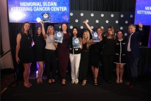 Group of ten people posing on stage at Memorial Sloan Kettering Cancer Center awards ceremony, holding 'Winner' signs.