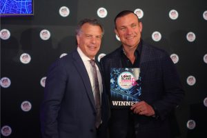Two men in suits pose at an awards event; one holds a WINNER plaque for Long Island Choice Awards.