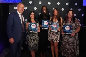Five people posing on a stage; four women and a man in a suit, each holding a 'WINNER' certificate for Long Island Choice Awards.