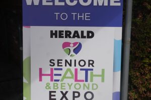 Public event sign reading 'WELCOME TO THE HERALD SENIOR HEALTH EXPO' on a colorful board outdoors.