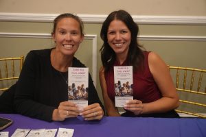 Two women sit at a table, smiling, each holding a brochure titled 'Care Is a Call Away.'