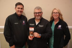 Three medical professionals posing together; the center person holds a brochure on brain aneurysm awareness.