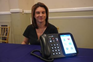 Smiling woman seated at a table with a large conference phone in the foreground on a blue tablecloth.