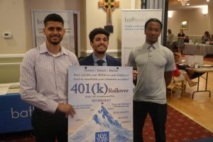 Three men pose with a large retirement-planning poster at a conference, with banners in the background.