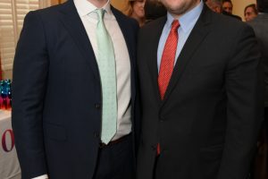 Two men in suits posing for a photo at a social reception, smiling at the camera.