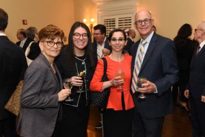 Four adults at a formal reception pose for a photo, each holding a drink and smiling.