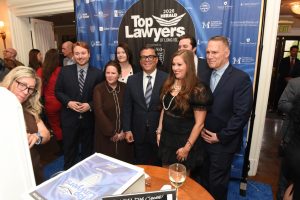 Group of well-dressed professionals posing for a photo at a 'Top Lawyers of Long Island' event in front of a blue sponsor backdrop.