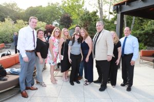 Group of adults posing together outdoors on a patio at a social event, smiling for a group photo.