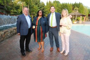 Four professionals posing by a pool and waterfall at an outdoor venue, smiling for the camera, dressed in business casual attire.