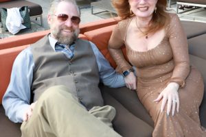 Smiling couple relaxing on an outdoor lounge sofa in a garden setting.