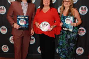 Three winners pose at a Long Island Choice Awards backdrop: man in brown suit with a WINNER plaque, two women with awards.