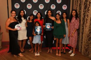 Group of eleven people in formal dresses posing with awards at a Long Island Choice Awards backdrop.