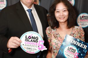 Two smiling award recipients pose at a step-and-repeat backdrop, each holding Long Island Choice Awards signs: a circular 5th anniversary sign and a blue WINNER certificate.