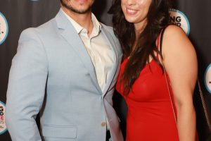 Smiling couple posing for a photo at the Long Island Choice Awards backdrop (man in a light blue suit, woman in a red dress).
