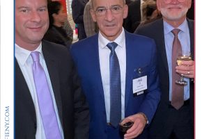 Three men in suits posing for a photo at a formal networking event, one holding a wine glass in the foreground