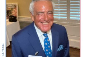 Smiling elderly man in a navy suit and blue tie at a law awards event, wearing a name badge.