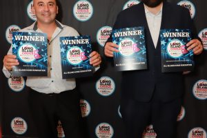 Two men stand side by side, smiling, holding WINNER plaques at the Long Island Choice Awards against a branded backdrop.