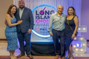 Four adults posing together in front of a Herald Long Island Choice Awards backdrop with a neon ring logo behind them.