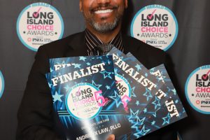 Smiling man in a black suit holds two blue 'Finalist' award certificates at a Long Island Choice Awards backdrop.
