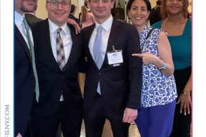 Five professionals in business attire pose for a group photo at a conference reception, with a 'Top Lawyers' banner above.