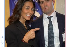 Smiling woman in a black blazer points at a man in a suit at a Top Lawyers event backdrop.