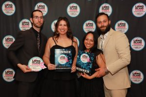 Group of four people at an awards event, two women hold winner plaques while posing in front of a branded backdrop with Long Island Choice Awards logos.