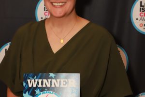 Smiling woman in an olive-green dress holds a 'WINNER' plaque for Long Island Choice Awards, Veterinarian, in front of a branded backdrop.