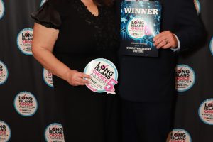 Two adults in formal wear pose at a Long Island Choice Awards backdrop; the woman holds a round award badge and the man holds a WINNER certificate.