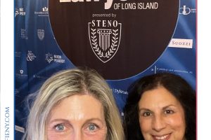 Two women smile for a selfie in front of a large 'Top Lawyers of Long Island' banner at the 2026 Herald event use backdrop.