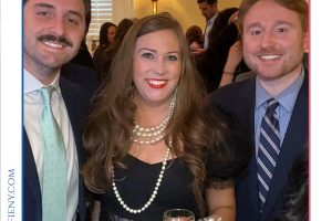 Three people pose for a formal event photo at a Top Lawyers of Long Island gathering; woman in the center wears pearls and a black dress, holding a wine glass.