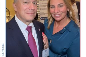Two professionals posing at a legal awards event: a man in a dark suit with a pink tie and a name badge, and a smiling woman in a teal blouse.