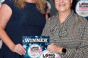 Two women pose at an awards ceremony; one holds a 'WINNER' plaque and a Long Island Choice Awards sticker in front of a branded backdrop.